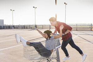 Verspieltes junges Paar mit Einkaufswagen auf dem Parkdeck - UUF12297