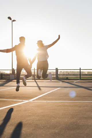Carefree young couple jumping on parking levelat sunset stock photo