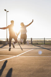 Carefree young couple jumping on parking levelat sunset - UUF12301