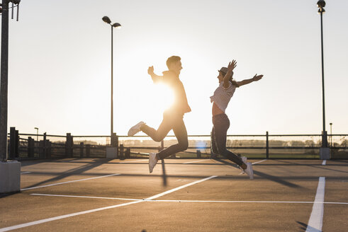 Carefree young couple jumping on parking levelat sunset - UUF12302