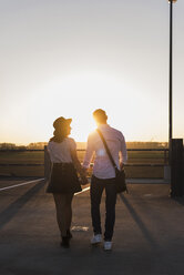 Junges Paar geht Hand in Hand auf dem Parkdeck bei Sonnenuntergang - UUF12308