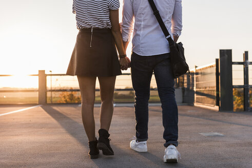 Young couple walking hand in hand on parking level at sunset - UUF12311