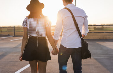 Young couple hand in hand on parking level at sunset - UUF12312