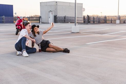 Glückliches junges Paar mit Motorroller auf einem Parkdeck, das ein Selfie macht - UUF12317