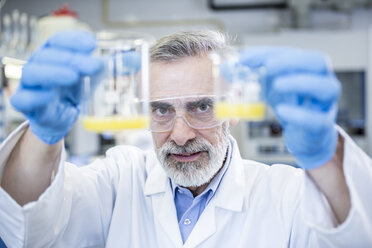 Scientist in lab holding up two beakers with liquid - WESTF23704