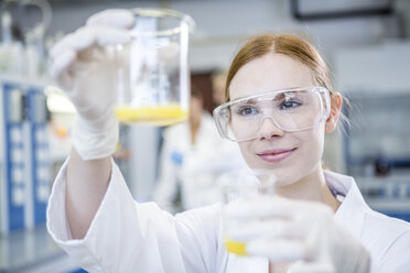 Scientist in lab holding up two beakers with liquid - WESTF23706