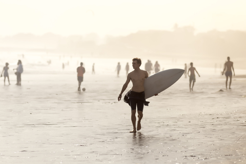 Indonesien, Bali, Surfer trägt sein Surfbrett am Strand bei Sonnenuntergang, lizenzfreies Stockfoto