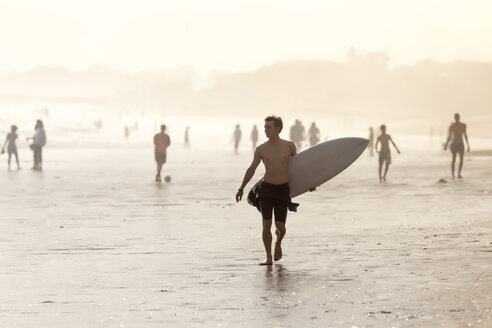 Indonesien, Bali, Surfer trägt sein Surfbrett am Strand bei Sonnenuntergang - KNTF00917