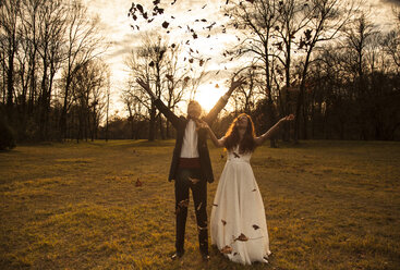 Happy bridal couple in park cheering and throwing leaves - FCF01309