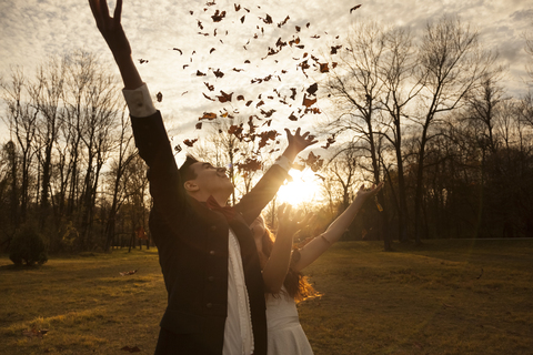 Glückliches Brautpaar im Park jubelnd und Blätter werfend, lizenzfreies Stockfoto