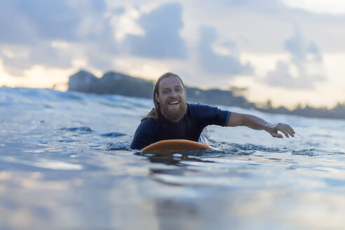 Porträt eines glücklichen Mannes auf einem Surfbrett auf dem Meer liegend - KNTF00925