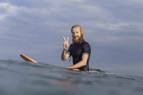 Porträt eines glücklichen Mannes, der auf einem Surfbrett im Meer posiert, lizenzfreies Stockfoto