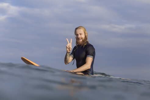 Porträt eines glücklichen Mannes, der auf einem Surfbrett im Meer posiert - KNTF00926