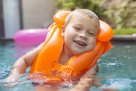 Porträt eines glücklichen Jungen mit Schwimmweste im Schwimmbad, lizenzfreies Stockfoto