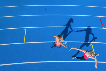 Top view of two female runners passing the baton on tartan track - STSF01423