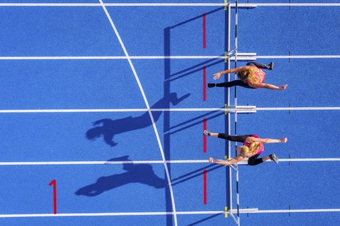 Top view of two female runners crossing hurdles on tartan track stock photo