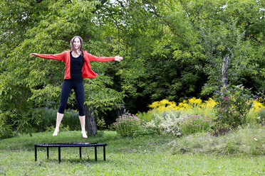 Lachende Frau, die auf einem Trampolin im Garten springt - NDF00694