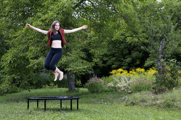 Frau springt auf Trampolin im Garten - NDF00695