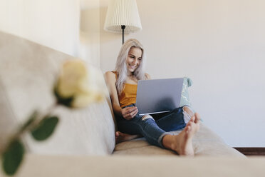 Smiling young woman using laptop on couch at home - GIOF03352