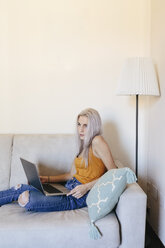 Young woman with laptop on couch at home - GIOF03353