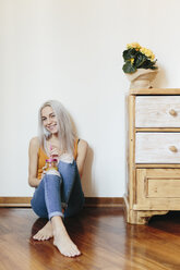Smiling young woman sitting on the floor at home - GIOF03359