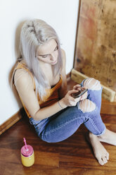 Young woman sitting on the floor at home using smartphone - GIOF03361