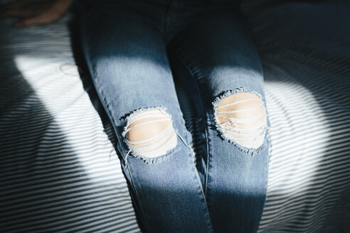 Close-up of woman sitting on bed at home wearing ripped jeans - GIOF03364