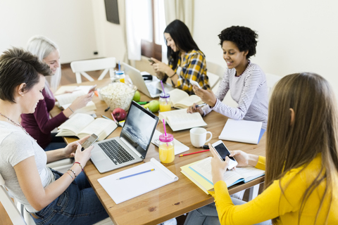 Gruppe von Studentinnen, die zu Hause am Tisch ein Handy benutzen, lizenzfreies Stockfoto