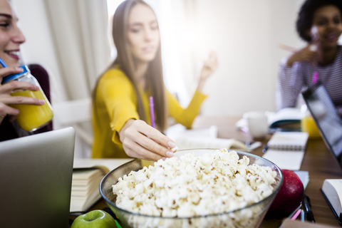 Studentin mit Freunden, die Popcorn aus einer Schüssel am Tisch zu Hause nehmen, lizenzfreies Stockfoto