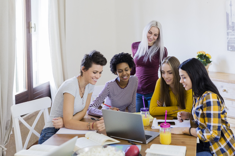 Gruppe von Studentinnen teilt sich einen Laptop am Tisch zu Hause, lizenzfreies Stockfoto