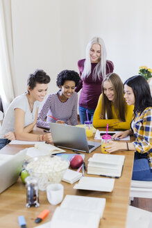 Gruppe von Studentinnen teilt sich einen Laptop am Tisch zu Hause - GIOF03386