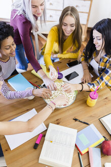 Freunde nehmen Popcorn aus einer Schüssel am Tisch zu Hause - GIOF03388