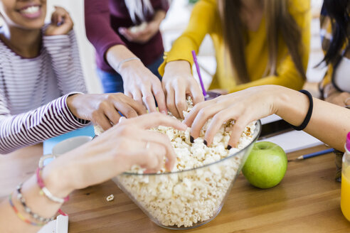 Freunde nehmen Popcorn aus einer Schüssel am Tisch zu Hause - GIOF03389