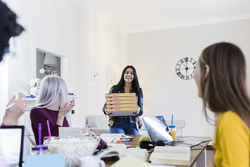 Young women bringing pizza for friends studying at home - GIOF03391