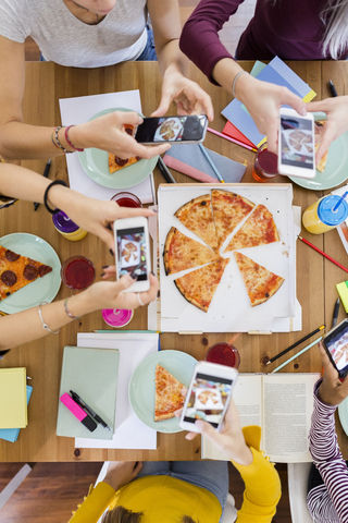 Gruppe junger Frauen, die zu Hause mit dem Handy fotografieren und sich eine Pizza teilen, lizenzfreies Stockfoto