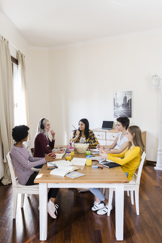 Gruppe von Studentinnen, die zu Hause am Tisch zusammenarbeiten, lizenzfreies Stockfoto