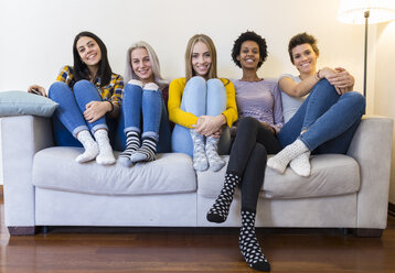 Portrait of group of female friends sitting on sofa in living room - GIOF03422