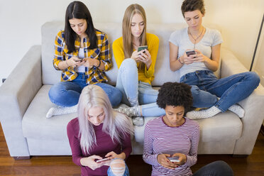 Group of female friends in living room obsessed by their smartphones - GIOF03426