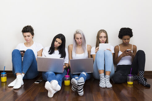 Gruppe von Freundinnen zu Hause, die auf dem Boden sitzen und Technik benutzen - GIOF03448