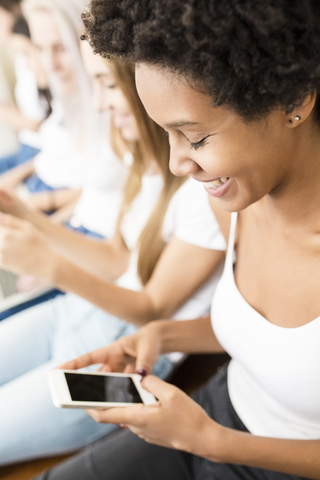 Lächelnde junge Frau mit Freunden, die ein Mobiltelefon benutzen, lizenzfreies Stockfoto