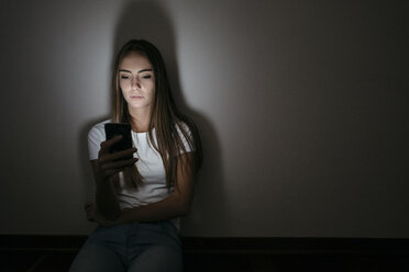 Young woman at home sitting on floor using cell phone in the dark - GIOF03457