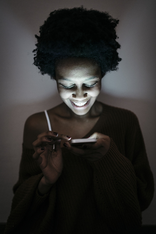 Smiling young woman using cell phone in the dark stock photo