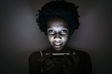 Porträt einer jungen Frau, die im Dunkeln ein Mobiltelefon benutzt - GIOF03460