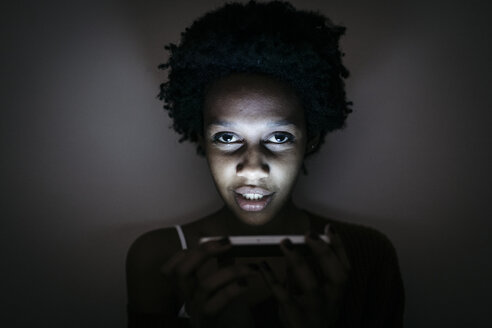 Porträt einer jungen Frau, die im Dunkeln ein Mobiltelefon benutzt - GIOF03460