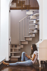 Young woman at home sitting on the floor using cell phone - GIOF03463