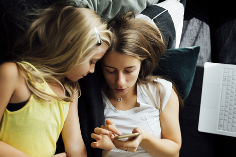 Relaxed mother and daughter with cell phone on sofa stock photo