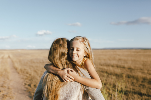 Lächelnde Tochter umarmt Mutter auf einem Feld, lizenzfreies Stockfoto