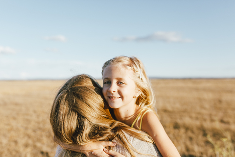 Porträt einer lächelnden Tochter, die ihre Mutter auf einem Feld umarmt, lizenzfreies Stockfoto