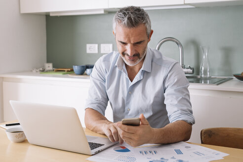 Mann, der Daten analysiert und Laptop und Mobiltelefon im Home Office benutzt - ALBF00249