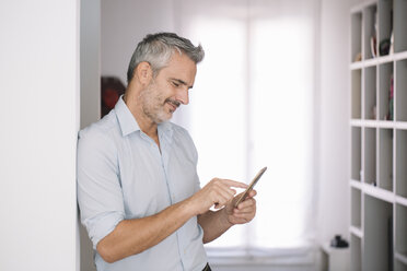 Smiling mature man using cell phone at home - ALBF00250